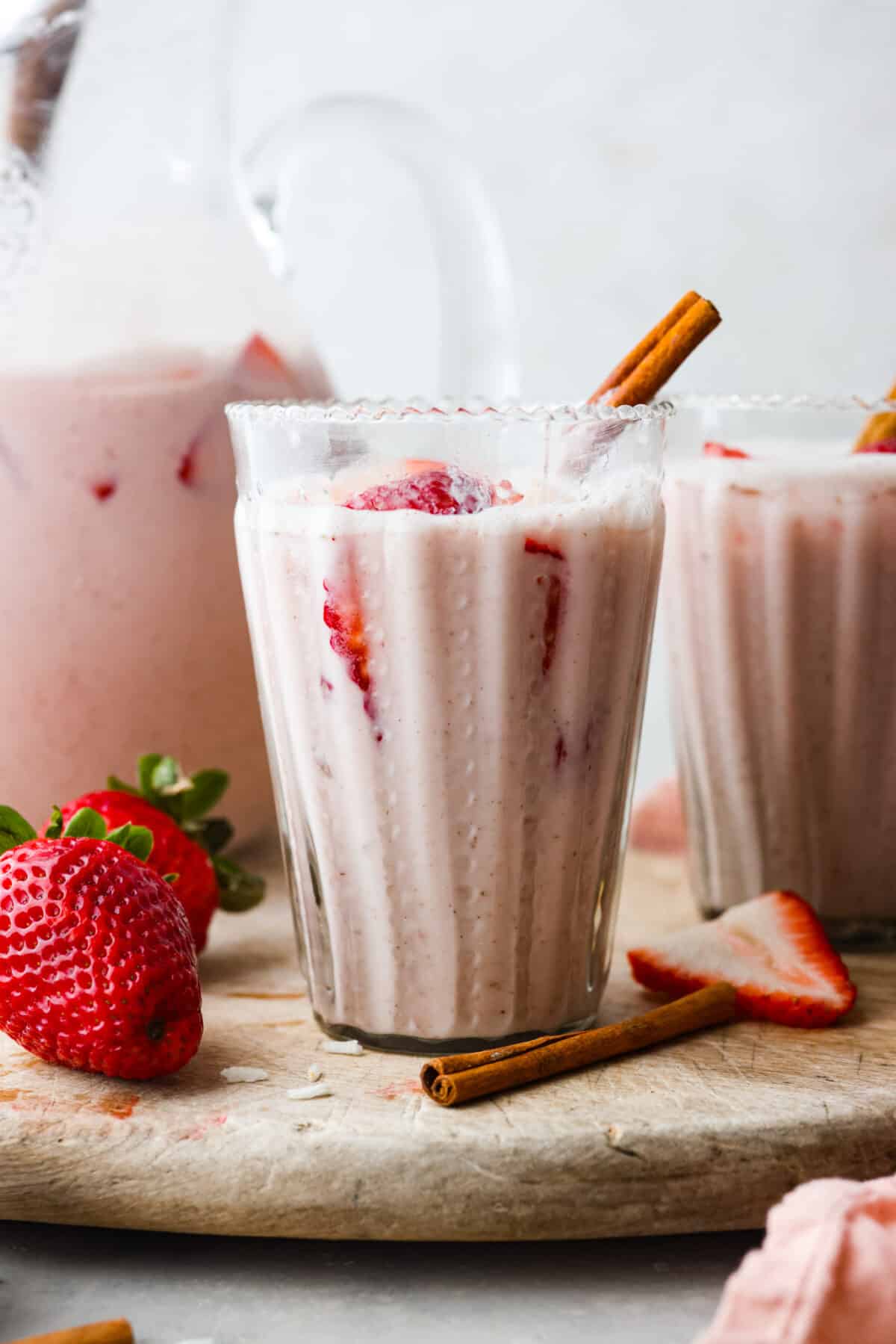Elevate the flavors of traditional horchata with this strawberry horchata recipe! It's a creamy drink soaked in rice water and cinnamon sticks, then sweetened with a strawberry puree. Everyone loves the strawberry version of this rich, milky Mexican drink! Close view of a glass of strawberry horchata with a pitcher behind it.